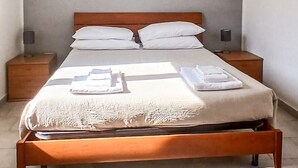 A bedroom with a wooden bed, two bedside tables, a large window, and a plain wall.