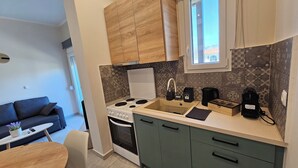 Een compacte keuken met een fornuis, spoelbak en moderne apparatuur, een eetgedeelte met tafel en stoelen, en uitzicht naar buiten door een raam.