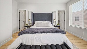 Ein modernes Schlafzimmer mit einem großen Bett, Nachttischen, einem Spiegel und einem Fenster mit Jalousien.