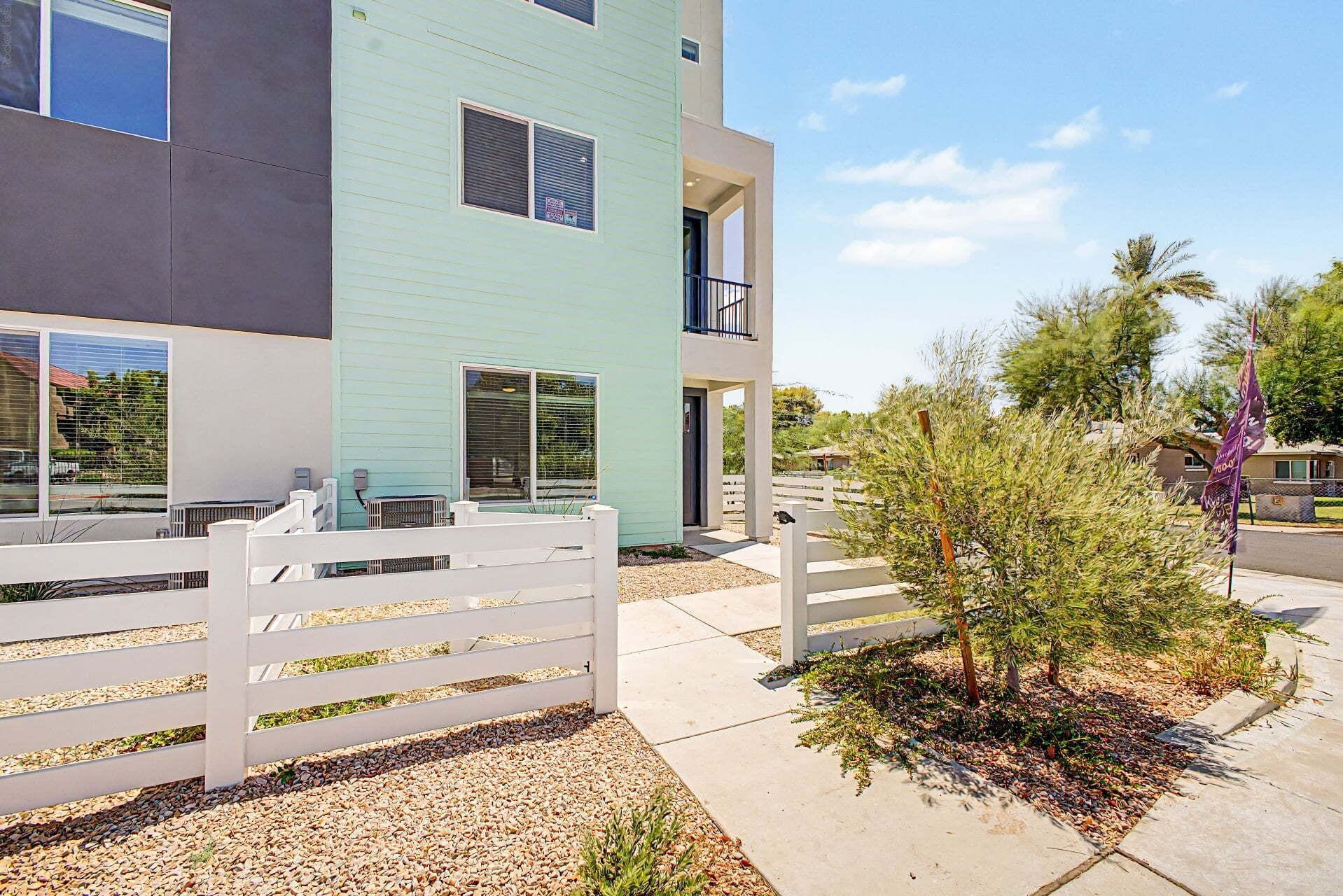 A modern two-story building with a light blue exterior, a white fence, and a small tree in the foreground.