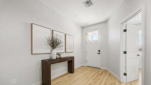 Ein Flur mit Holzdielen, einer weißen Tür und zwei gerahmten Kunstwerken an der Wand.