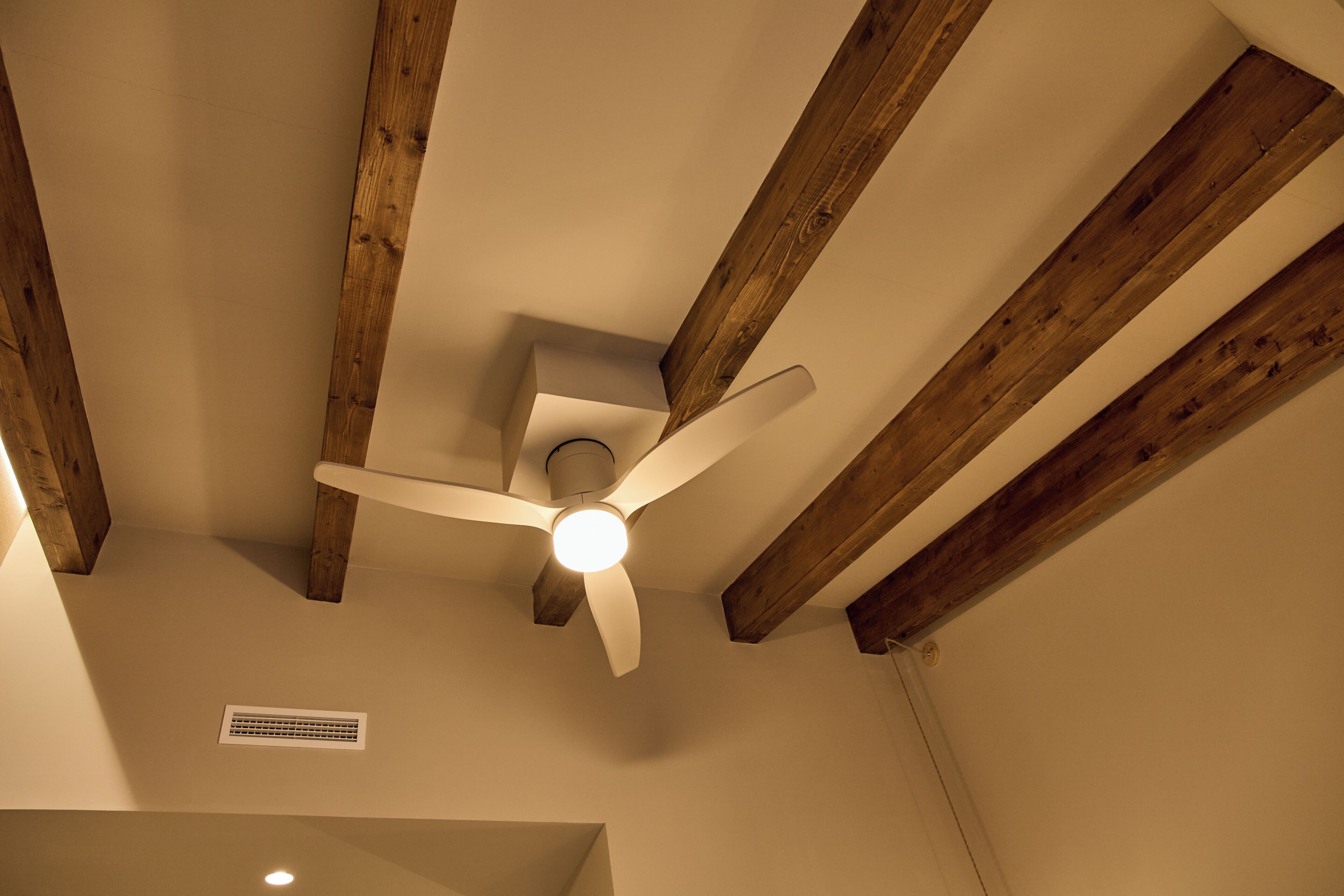 A ceiling fan with wooden beams, a vent, and a light fixture.