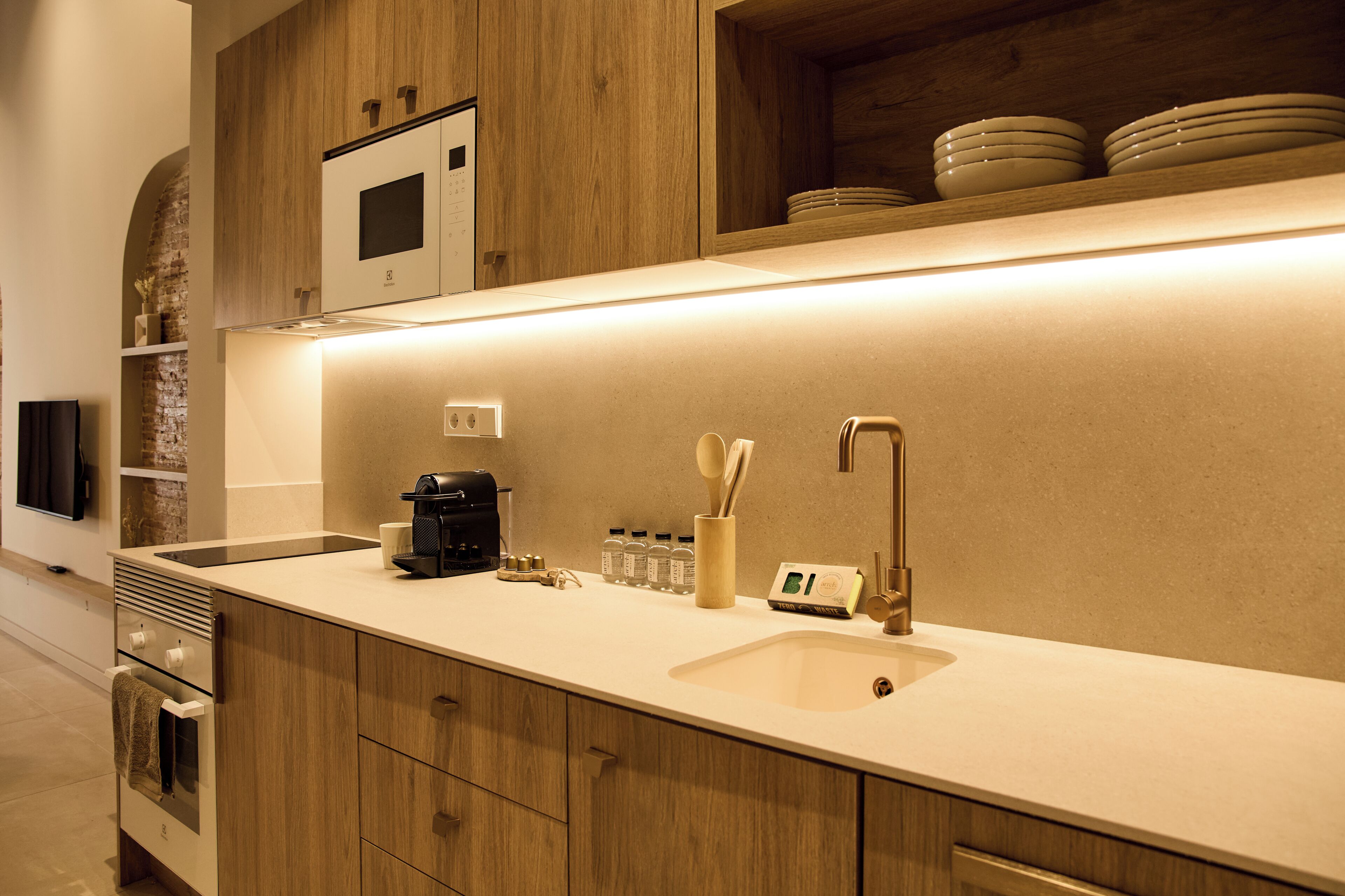 A modern kitchen with wooden cabinets, a built-in microwave, a coffee maker, and a sink.