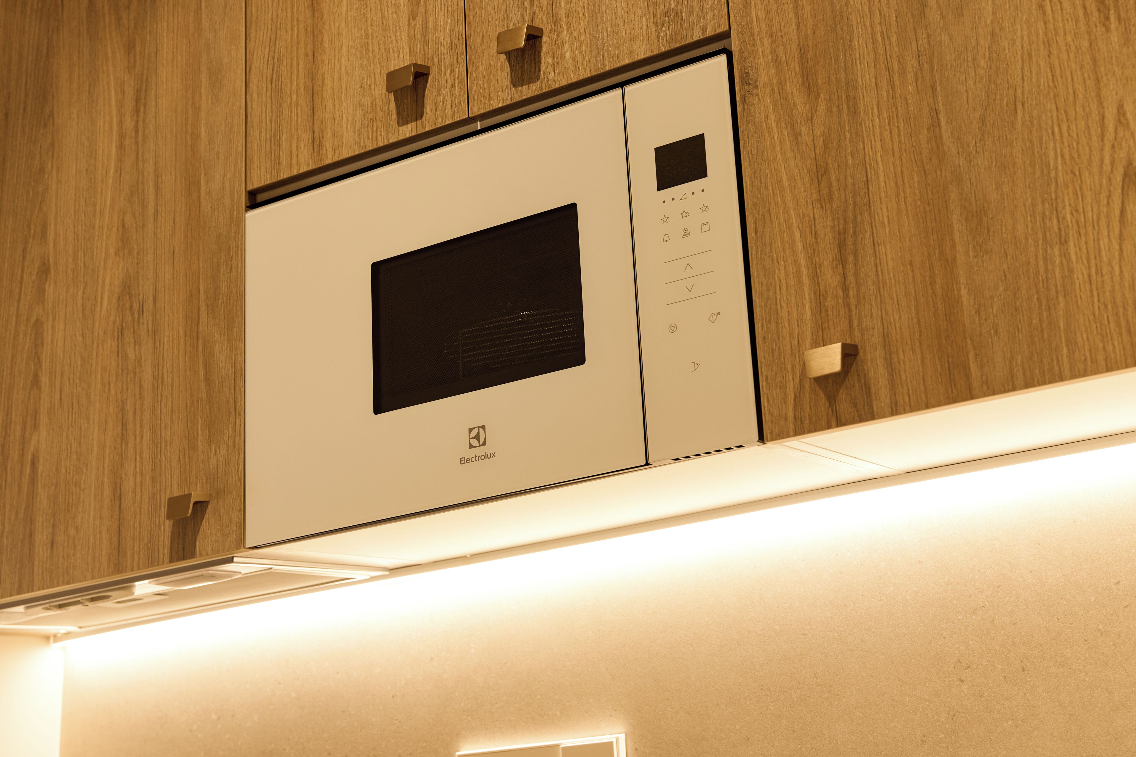 Un microondas empotrado en la pared, con panel de control digital, dentro de una cocina con muebles de madera.