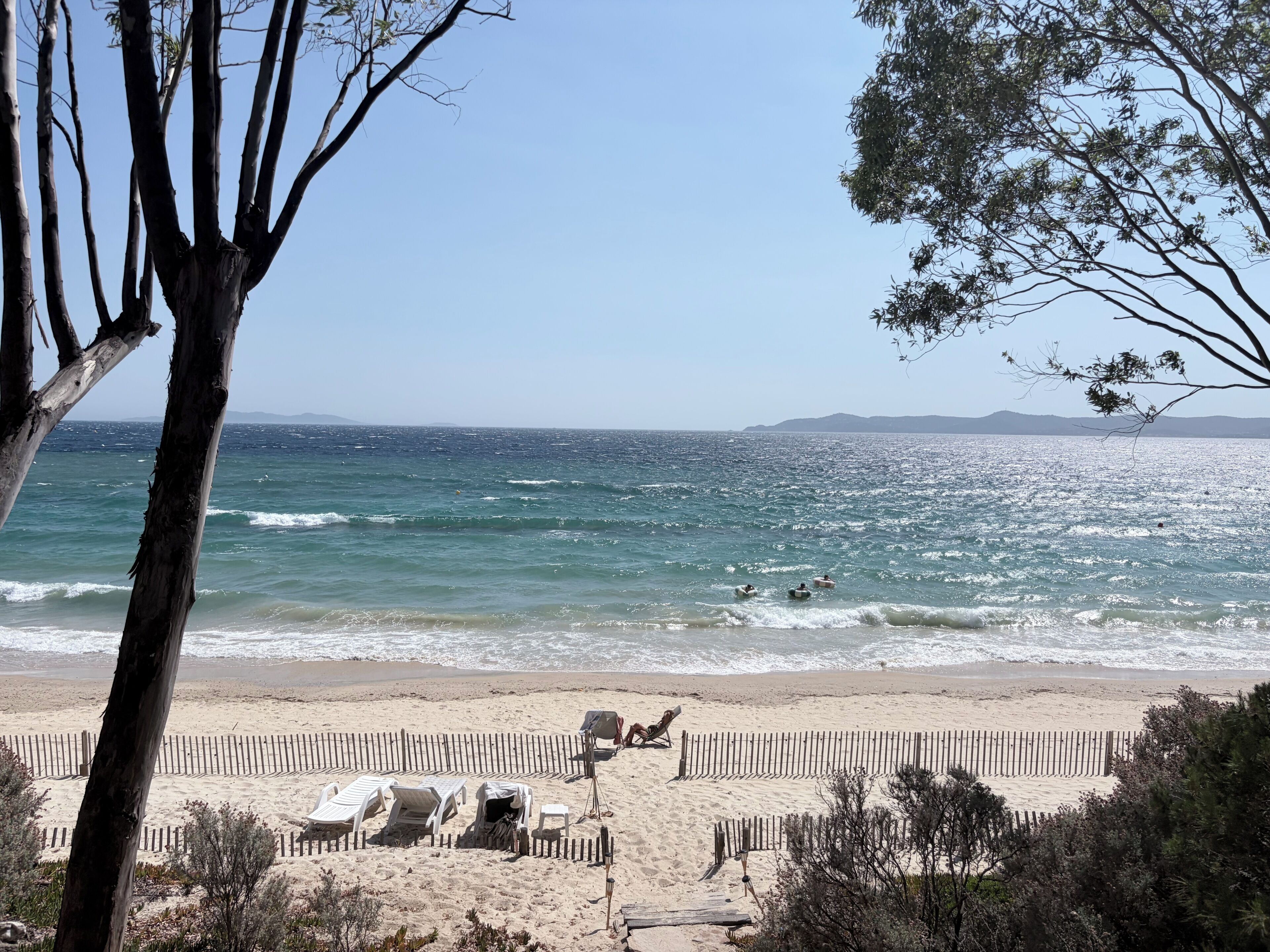 A beach with a wooden fence, sun loungers, and a clear view of the ocean.