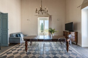 A dining room with a checkered floor, a chandelier, a dining table with chairs, a sofa, a television, and a cabinet. - Tenuta Santo Spirito - Wine Farm in a Historic Villa (Vittoria)