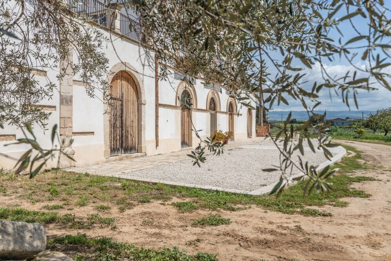 Edifici amb finestres i portes d'arc, un camí de grava i vista del paisatge.