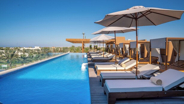 A poolside area with sun loungers and umbrellas, a clear blue pool, and a view of the landscape.