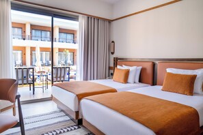 A hotel room with two beds, a view of the outdoor seating area, and a balcony.