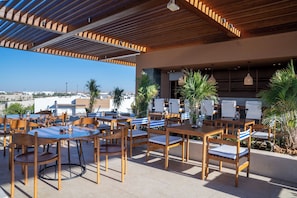 An outdoor seating area with multiple tables and chairs, a view of the cityscape, and a covered roof structure.