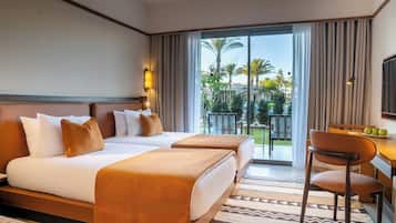 A hotel room with a bed, a desk, a chair, a TV, and a balcony with a view of palm trees.