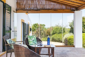 A covered patio with wicker furniture, a table with glasses and a bottle, and a view of greenery. - New! Quinta Salicos | Large Pool & Near Carvoeiro (Salicos)