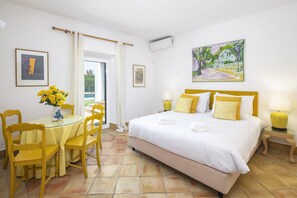 A hotel room with a bed, a table with chairs, a vase of flowers, and a painting on the wall. - New! Quinta Salicos | Large Pool & Near Carvoeiro (Salicos)