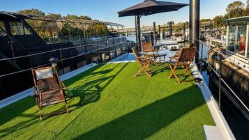 Een dakterras met kunstgras, houten lounge fauteuils en een grote parasol.