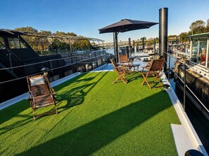 A rooftop deck with artificial grass, wooden lounge chairs, and a large umbrella.