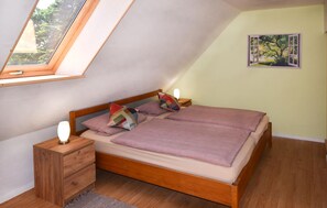 Une chambre avec un plafond en pente, un lit avec un cadre en bois, deux tables de chevet avec des lampes et un tableau accroché au mur.