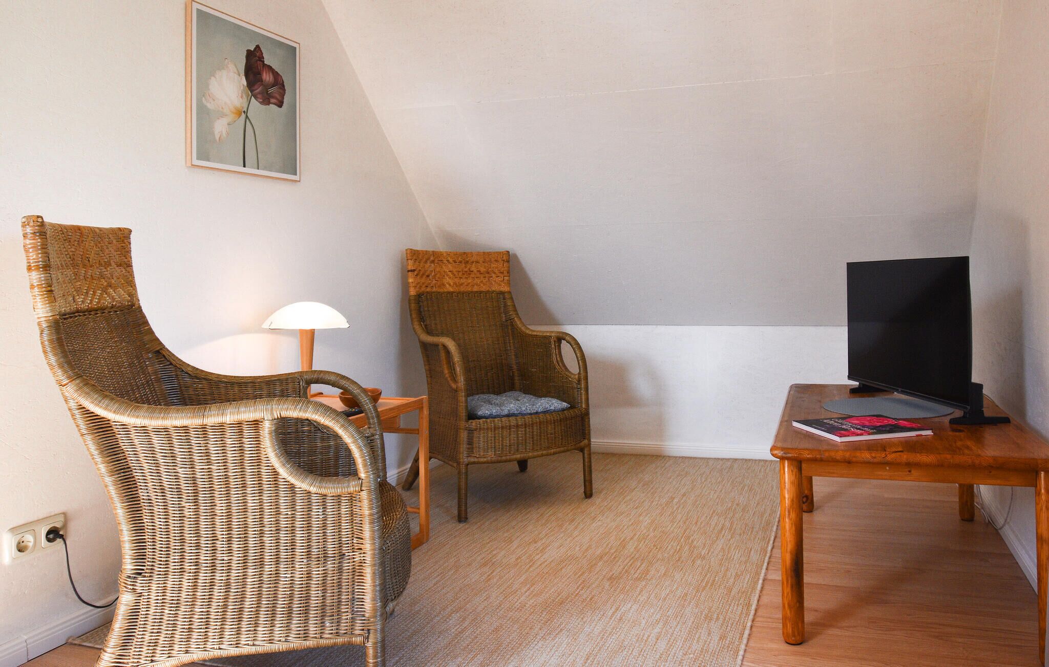 A small room with two wicker chairs, a wooden table, a TV, and a lamp.