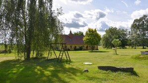A grassy area with a swing set, a stone, and a building with a red roof. - Gorgeous home in Dobbertin with WiFi (Dobbertin)