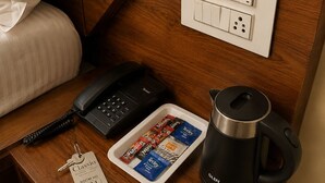 A hotel room with a wooden nightstand, a black telephone, a tray with snack packets, a black kettle, and a keychain with a room number. - Hotel Classio (Balichauki)