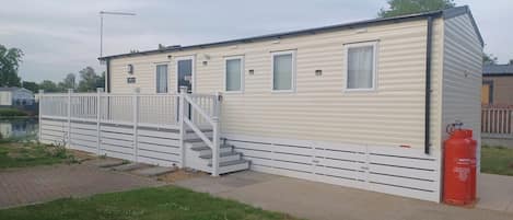 A mobile home with a white exterior, a set of stairs leading to a door, and a red fire extinguisher on the ground.