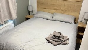 Una cama bien hecha con cabecera de madera, dos mesitas de noche con lámparas y un radiador.