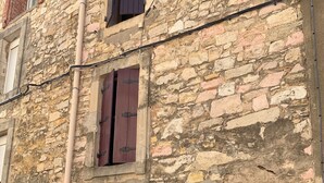Un bâtiment en pierre doté d’une grande entrée en arc de cercle et d’une porte rouge, d’une petite fenêtre avec des volets et d’une enseigne portant le chiffre « 5 ».