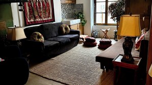 Un salon avec un canapé noir, un tapis à motifs, un plancher en bois, un lustre, une lampe et une fenêtre donnant sur un beau paysage.