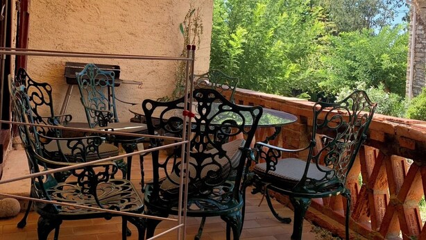 Une terrasse extérieure avec une table et des chaises, une pergola en bois et un mur en pierre.