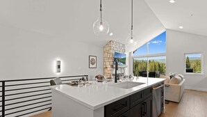 A modern kitchen with a large island, pendant lighting, and a view of the outdoors. - Downtown WP Sojourn Villa 115 | Bunk Room | Great Views | Discounted Attractions (Winter Park)