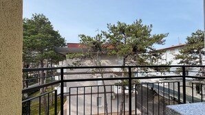 A balcony with a metal railing, a stone ledge, and a view of a building with a red roof and trees. - Great flat with two terraces and parking (Bibione)