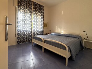 A bedroom with a bed, curtains, a nightstand, and a wall-mounted lamp. - Great flat with two terraces and parking (Bibione)