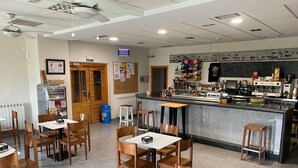 A restaurant with multiple tables and chairs, a bar area with a counter, and various food and drink items displayed. - EL MENSARIO (Campisábalos)