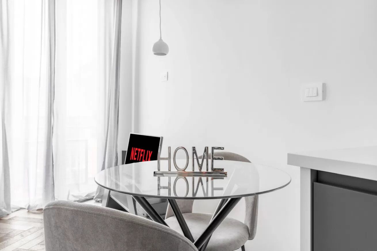 Ein modernes Zimmer mit Glastisch, Stuhl, Pendelleuchte und einem Schild mit der Aufschrift 'NETFLIX HOME'.