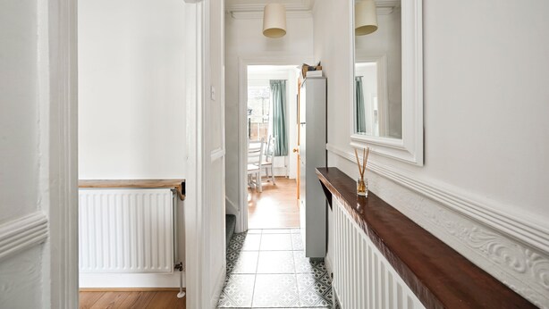 A hallway with a radiator, a wooden floor, a mirror, and a door leading to another room. - Host My Nest: 2-Bed w/ Garden Near Forest Gate (london)