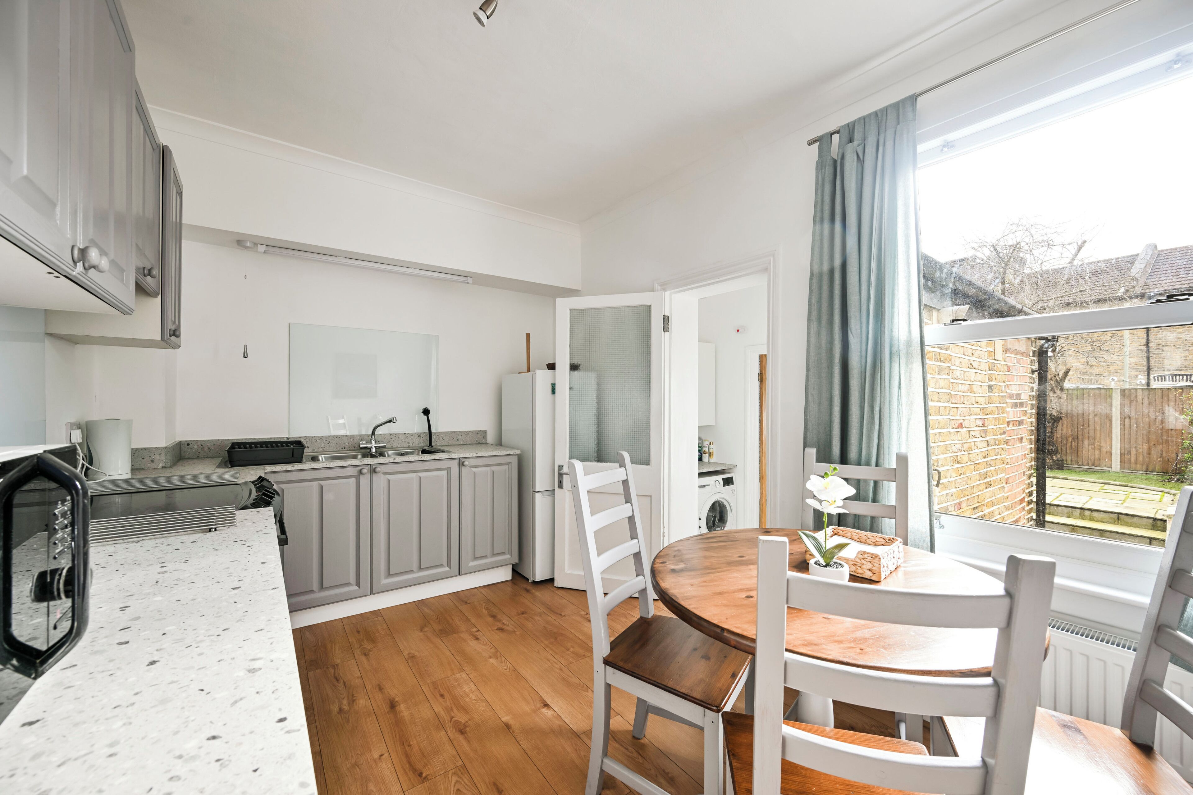 A modern kitchen with grey cabinets, a wooden dining table, and a view of a brick garden.