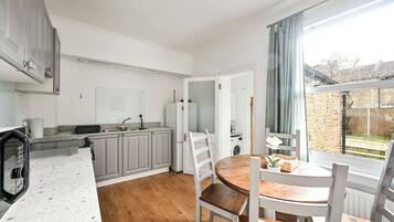 A modern kitchen with grey cabinets, a wooden dining table, and a view of a brick garden.