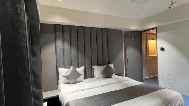 A modern hotel room with a large bed, a grey headboard, and a blue carpet. - Hotel NR INN (Ahmedabad)