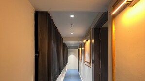 A hotel hallway with a blue carpet, wooden paneling on one side, and framed pictures on the walls. - Hotel NR INN (Ahmedabad)