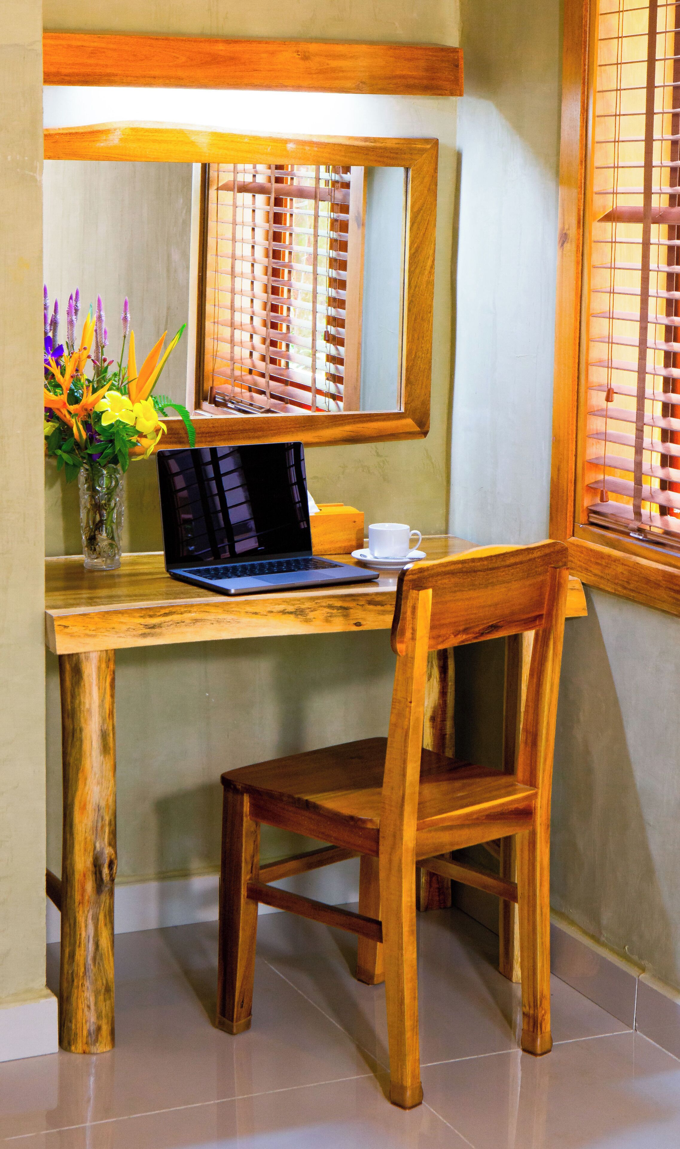 Uma mesa de madeira com um laptop, uma chávena e um vaso com flores.