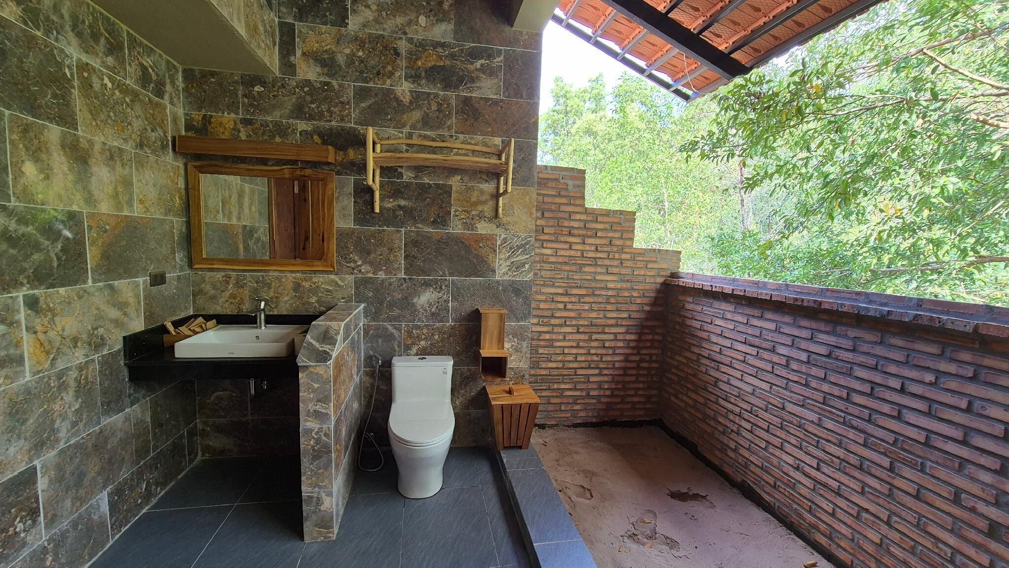 A bathroom with a stone wall, a wooden-framed mirror, a sink, and a toilet.