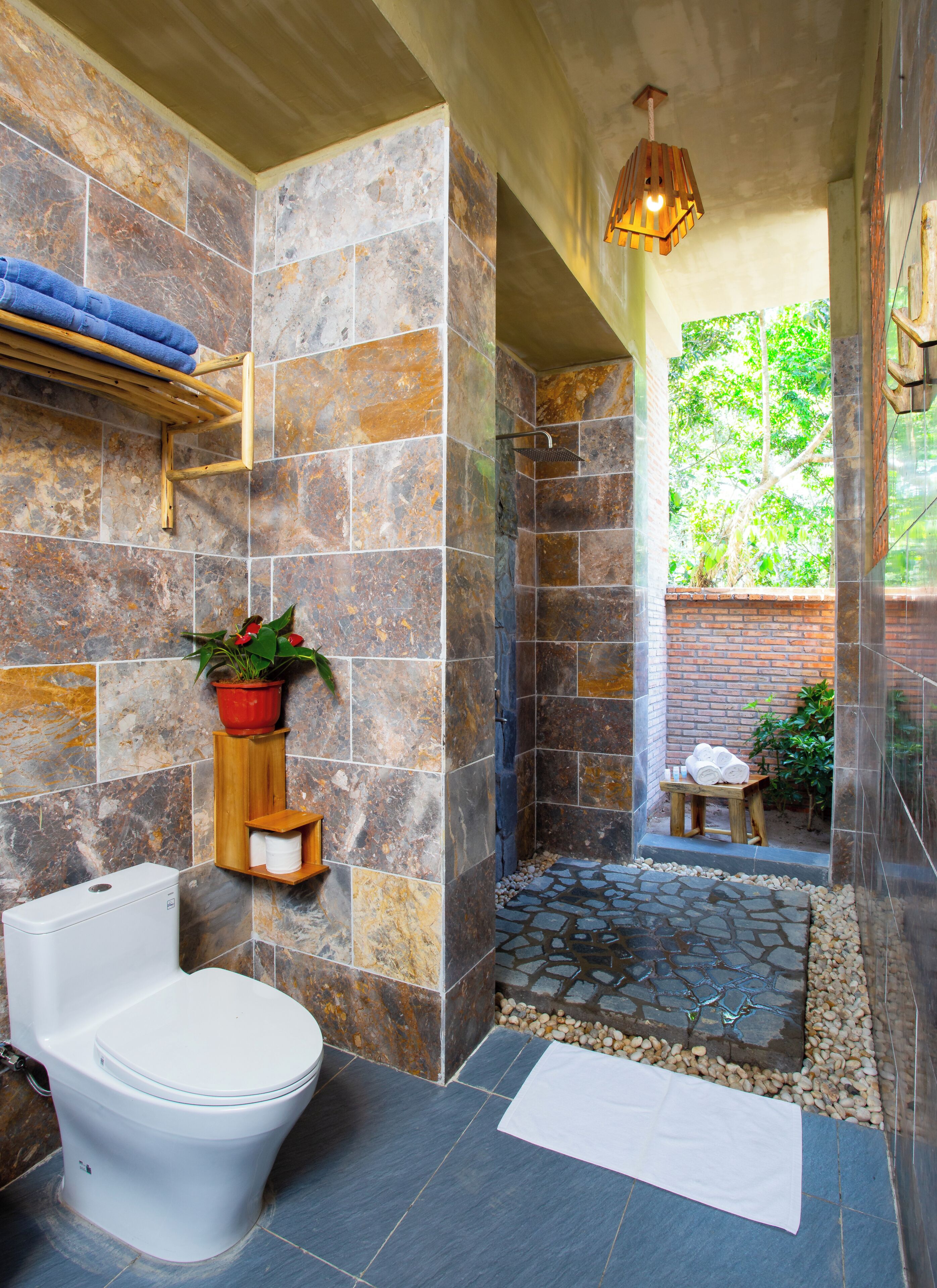 A bathroom with a toilet, a shower area, and a small seating area with a potted plant.