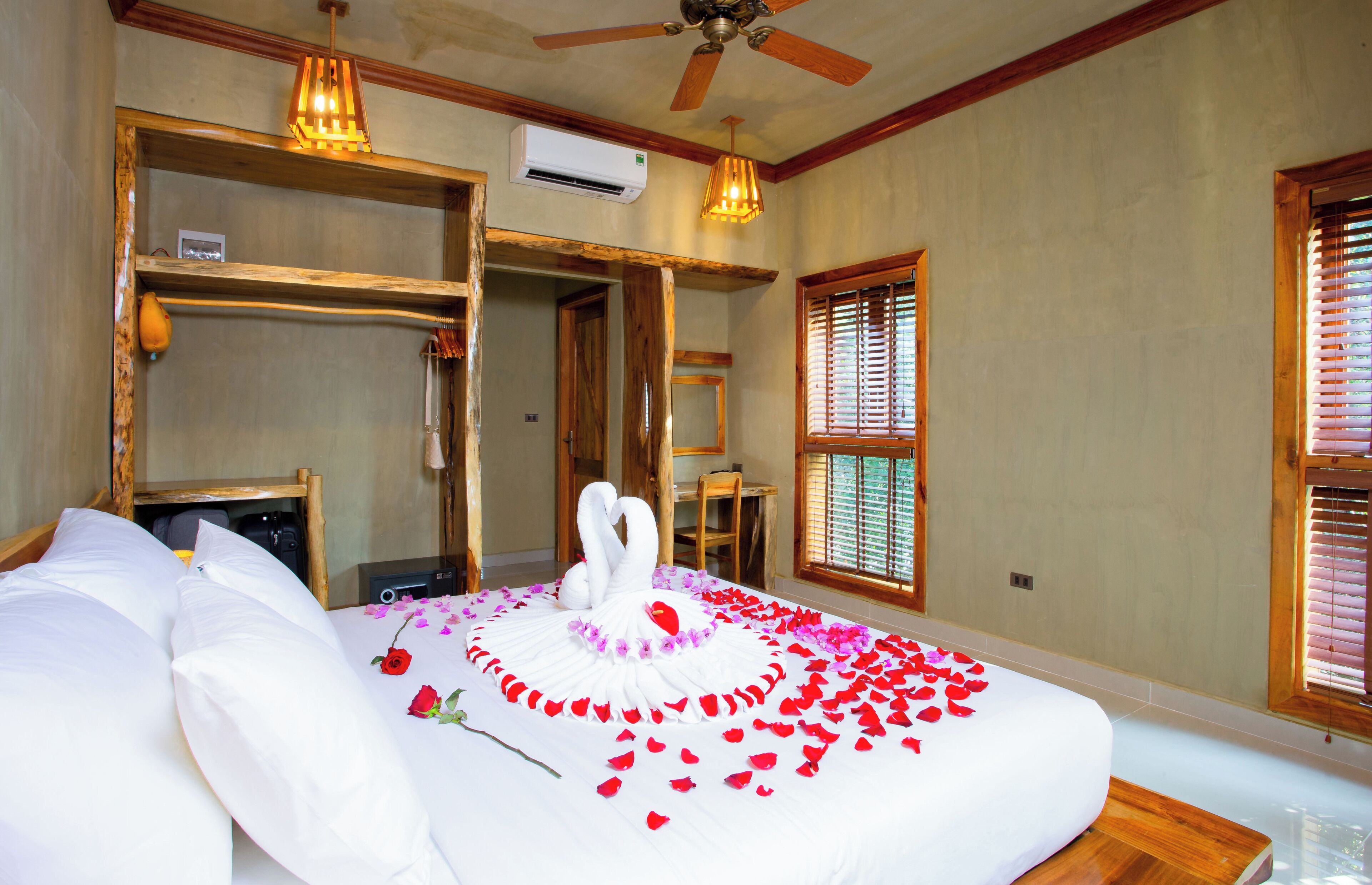 Una habitación de hotel con cama, ventilador de techo, aire acondicionado, muebles de madera y una ventana con persianas.