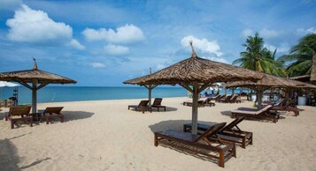 Una playa con sombrillas de paja y sillones de madera.