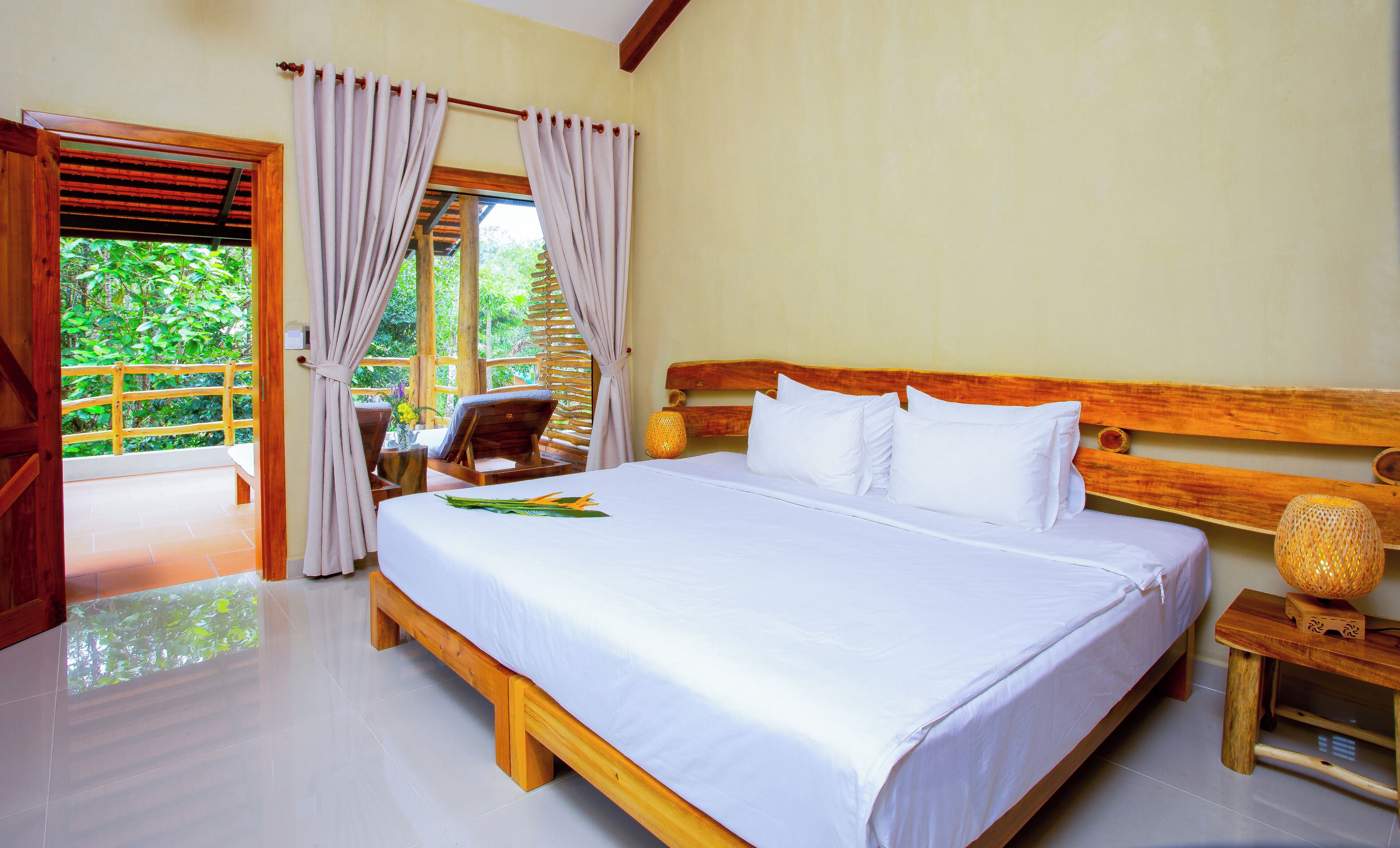 A hotel room with a large bed, wooden headboard, and a view of greenery through the window.