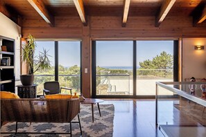 Ein modernes Interieur mit Holzboden, großen Schiebeglastüren, einem Korbsessel und Blick ins Freie.