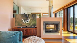 A modern living room with a television displaying 'Portugal Active,' a fireplace, and a view through large windows. - Sunrise Escape with Pool by Portugal Active (Viana do Castelo)