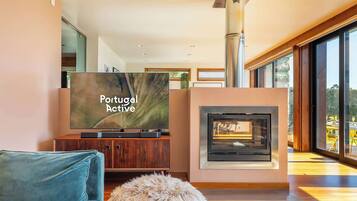 A modern living room with a television displaying 'Portugal Active,' a fireplace, and a view through large windows.