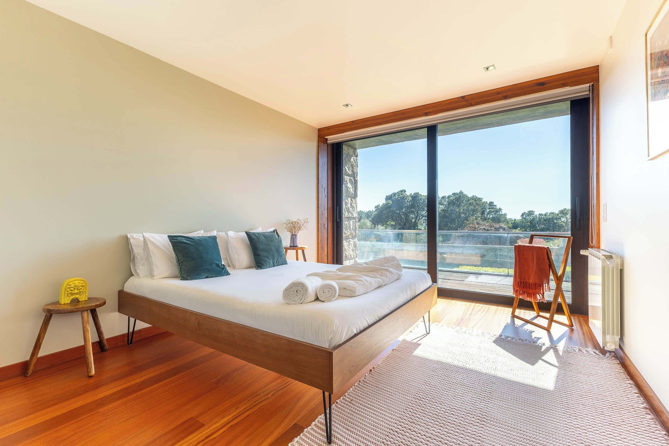 Un dormitorio moderno con una cama grande, una mesita auxiliar pequeña, una silla y vistas al exterior.
