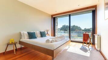 Un dormitorio moderno con una cama grande, una mesita auxiliar pequeña, una silla y vistas al exterior.