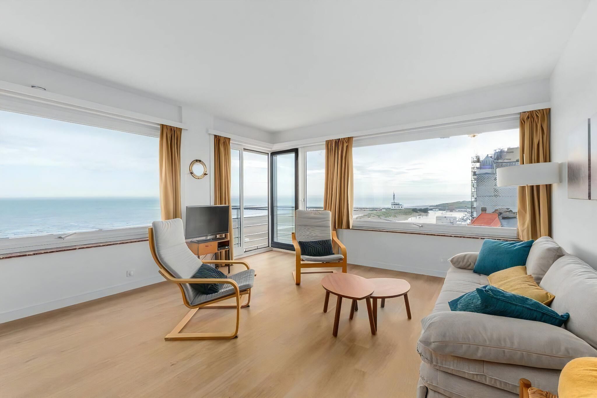 Ein modernes Wohnzimmer mit einer Couch, Sesseln, einem Fernseher und Blick aufs Meer.